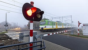 Przejazd z opuszczonymi szlabanami i sygnalizatorem, przejeżdżający pociąg.