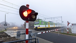 Pociąg na przejeździe, zamknięte rogatki, pulsujące światło