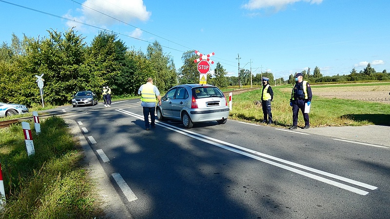 Przedstawiciele kampanii i policjanci podczas akcji prewencyjnej wręczają materiały kierowcy oczekującemu przed przejazdem.
