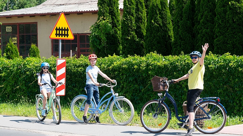 mama z dziećmi na rowerach przy znaku A-9 przejazd kolejowy z zaporami.